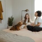 woman in white long sleeve shirt sitting on bed beside brown dog